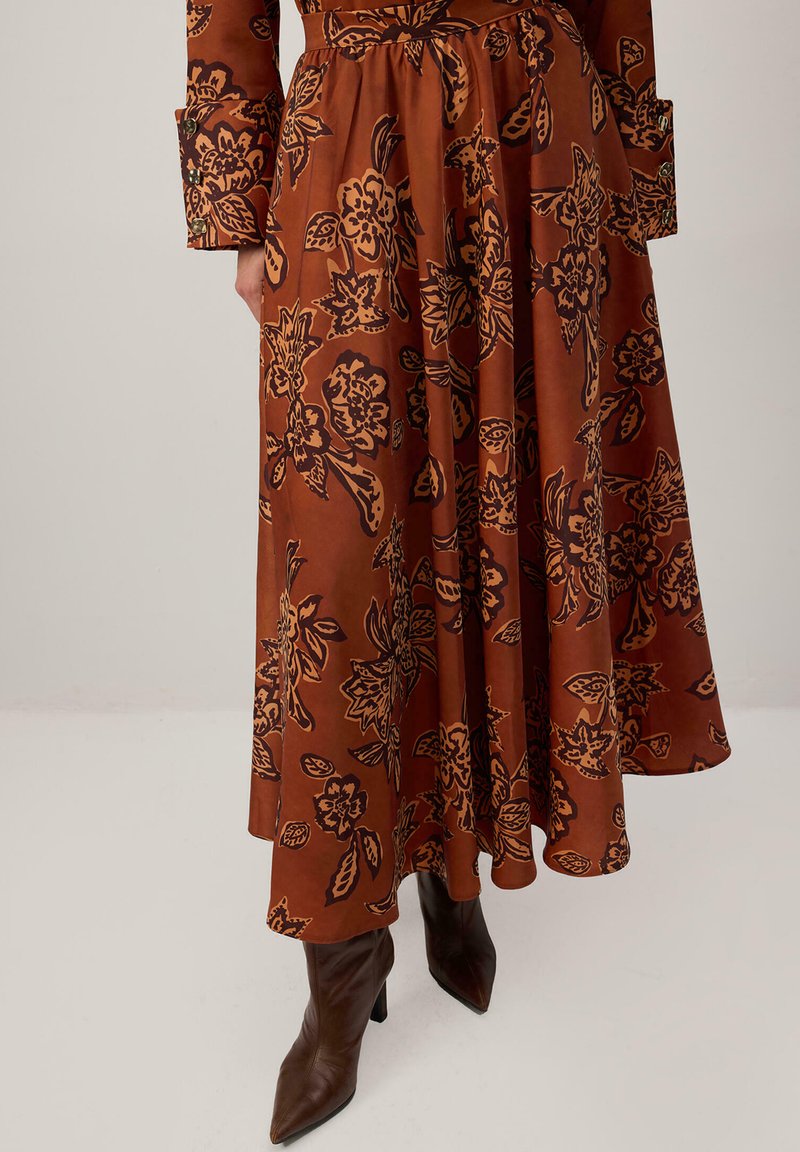 Falda floral marrón con patrones florales negros llamativos, diseño fluido, tela ligera, cintura ceñida, combinada con botas de tacón puntiagudas marrones.