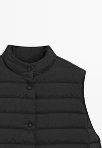 Smanicato imbottito nero con collo alla coreana, caratterizzato da pannelli trapuntati orizzontalmente e due chiusure con bottoni sul davanti. Tessuto leggero.