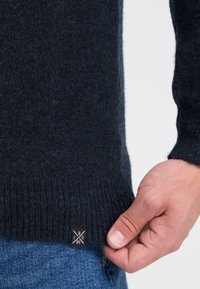 Dunkelblauer Pullover aus weichem Strickmaterial, mit gerippten Bündchen und Saum sowie einem kleinen Markenzeichen auf der unteren linken Seite.