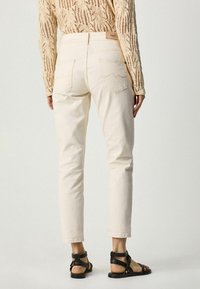 Jeans beige clair avec une coupe droite, dotés de poches plaquées et de détails de couture subtils. Portés avec des sandales noires à lanières.