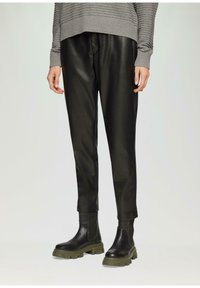 Zwarte neplederen broek met een gladde textuur, tapered design en boorden. Gepaard met chunky zwarte laarzen met olijfgroene zolen.