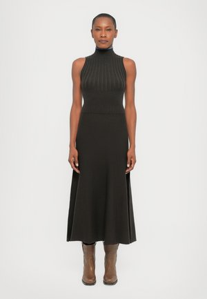 Black ribbed knit dress with a high neckline and a flared skirt. Features side slits and paired with brown ankle boots.