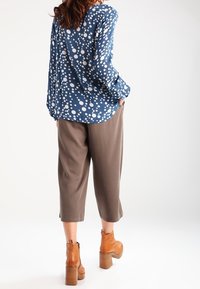 Blusa blu con pois bianchi, vestibilità ampia, maniche lunghe; pantaloni cropped color taupe; stivaletti marroni con tacco spesso.