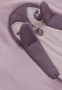Paarse katoenstof heeft een geborduurd pinguïnontwerp met textuuraccenten en lichte stikdetails op een lichte achtergrond.