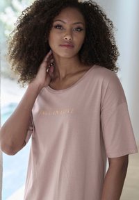 Light pink oversized t-shirt made from soft fabric, featuring "FALL IN LOVE" printed in gold. Short sleeves and a relaxed fit.