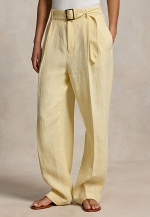 Pantaloni galbeni din in, cu talie înaltă, curea lată și cataramă, purtați cu un top alb și sandale plate maro.
