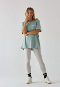 Jasnoniebieska, oversize'owa koszulka z logo, w połączeniu z dopasowanymi białymi legginsami i białymi trampkami w czarno-białe paski.
