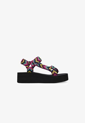 Sandalias de plataforma negras con una correa tejida colorida en un patrón de chevron en rosa, azul y amarillo; diseño anudado para un detalle adicional.