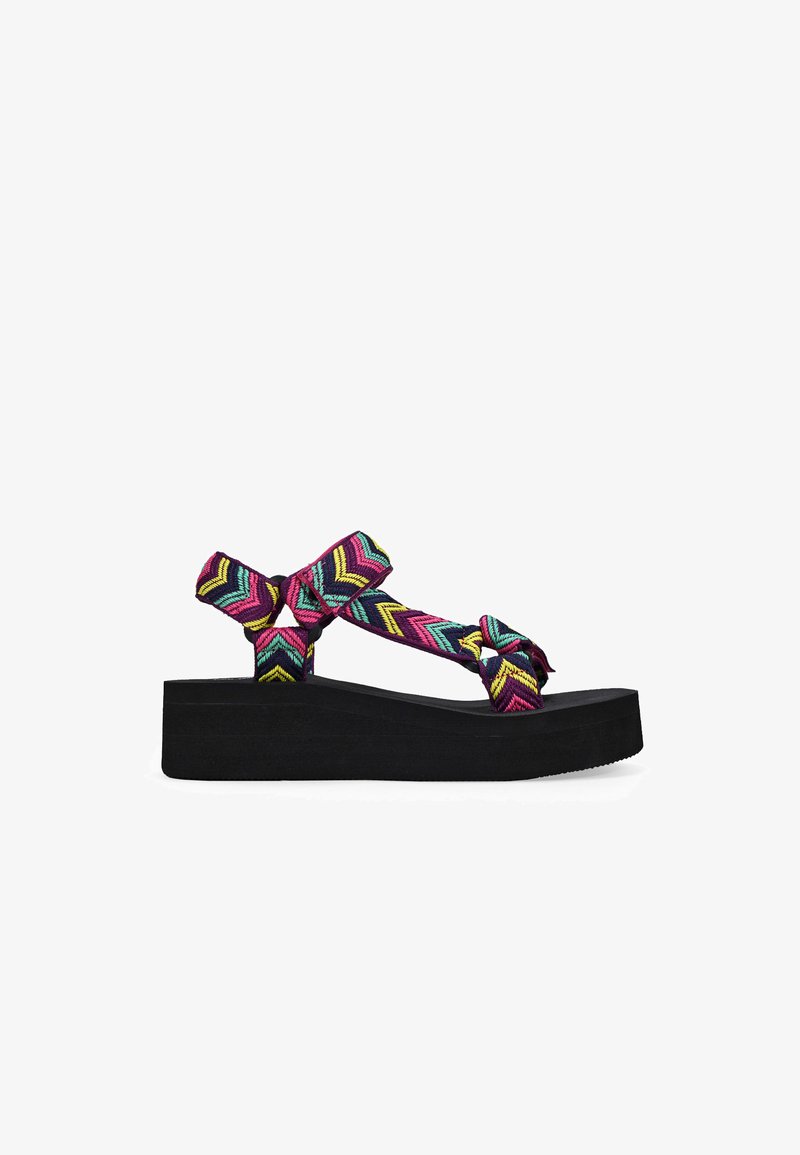 Sandalias de plataforma negras con una correa tejida colorida en un patrón de chevron en rosa, azul y amarillo; diseño anudado para un detalle adicional.