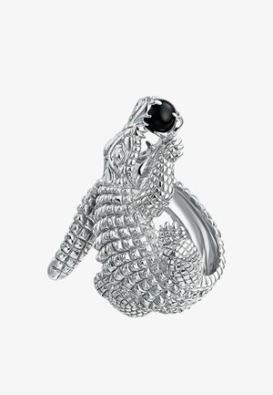 Anillo de plata diseñado como un cocodrilo, con escamas detalladas y una piedra preciosa negra en su boca. Superficie suave y brillante con patrones intrincados.