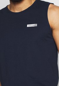 Canottiera blu navy in cotone, con scollatura rotonda e un'etichetta logo bianca sul petto. Tessuto morbido, design senza maniche.