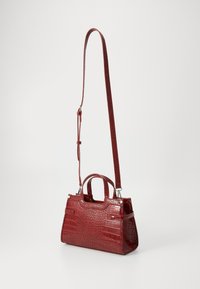 Sac à main rouge en cuir embossé crocodile avec double poignées et une bandoulière amovible, présentant un design structuré et une finition brillante.