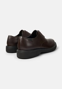 Pantofi din piele maro cu un finisaj neted, vârf rotunjit și talpă din cauciuc negru. Prezintă șireturi maronii și un design minimalistic, fără branding vizibil.