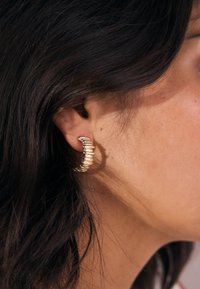 Gold earrings in a coiled design, featuring multiple rounded segments. The texture is smooth, with a polished shine.