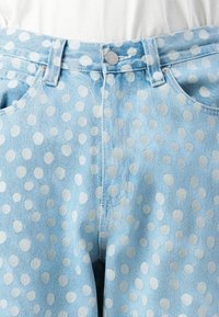 Light blue denim jeans with white polka dots, front pockets, belt loops, and a silver button closure worn with a white top.