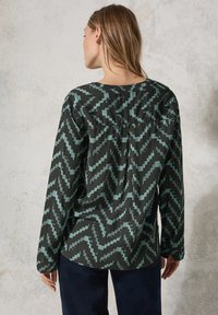 Camicia a maniche lunghe con un motivo a zigzag in teal e nero. Presenta un colletto rotondo e dettagli arricciati sul retro. Tessuto liscio.