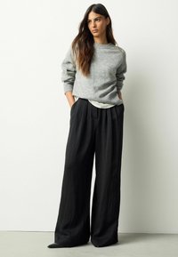 Pulover gri tricotat cu guler rotund și croială lejeră, asortat cu pantaloni negri cu picior larg. Textură moale; design minimalist.