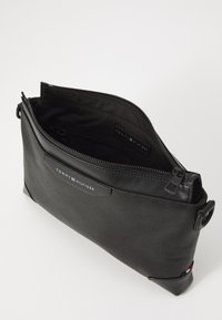 Black Tommy Hilfiger pouch made of textured fabric with a smooth leather trim. Features a zip closure and embossed logo on the front.