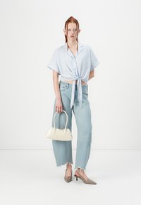Blusa azul claro com riscas, de mangas curtas e atada, combinada com uns jeans azuis claros de cintura alta, sapatos de salto bejes com tiras atrás e uma pequena bolsa branca.