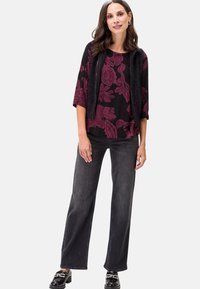 Top floreale nero con motivo bordeaux, abbinato a jeans svasati scuri e scarpe nere. Il top presenta maniche a tre quarti e una vestibilità rilassata.