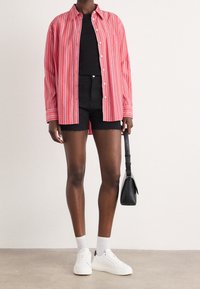 Red and white striped button-up shirt, black fitted shorts, white sneakers and ankle socks, with a small black shoulder bag.