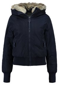 Veste d’hiver bleu marine avec fermeture éclair devant, deux poches zippées, poignets et ceinture côtelés, et une capuche bordée de fausse fourrure beige et crème.