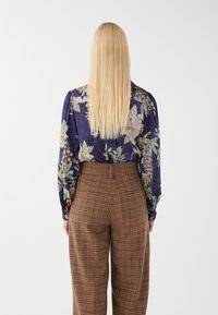 Blusa con motivo floreale in blu navy con dettagli verde chiaro e rosa. Pantaloni con stampa a quadri marroni a vita alta, dotati di tasche frontali e una vestibilità strutturata.