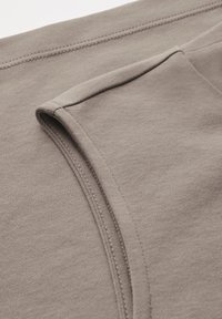 Tessuto di felpa marrone chiaro con una texture liscia, cuciture visibili e orlo rinforzato. Design minimalista senza motivi o accessori.