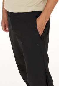 Mustat ulkoiluhousut, jotka on valmistettu kestävästä kankaasta. Housuissa on vetoketjulliset sivutaskut ja istuva malli, jossa on teksturoitu pinta.