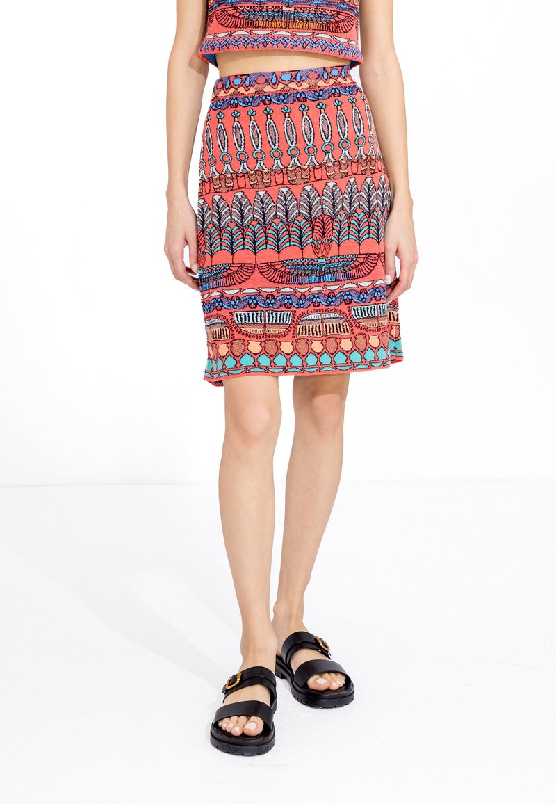 Rood-oranje gebreide crop top en bijpassende rok met meerkleurige patroon details. Gedragen met zwarte sandalen met een gouden gesp.