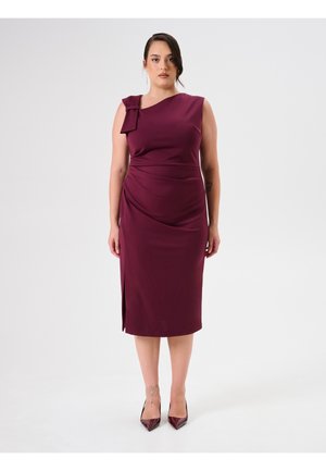 Bordeauxrotes Kleid mit diagonaler Halslinie und Schulterbogen-Detail. Es hat eine figurbetonte Silhouette mit seitlichem Rüschen und einem hohen Schlitz bis zum Oberschenkel.