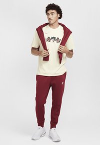 Light yellow t-shirt with floral graphic, maroon hoodie draped over shoulders, maroon sweatpants, and white athletic shoes.