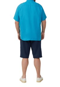 Lichtblauw linnen overhemd met korte mouwen en een rechte snit, gecombineerd met donkerblauwe shorts. Witte sneakers maken de outfit af.