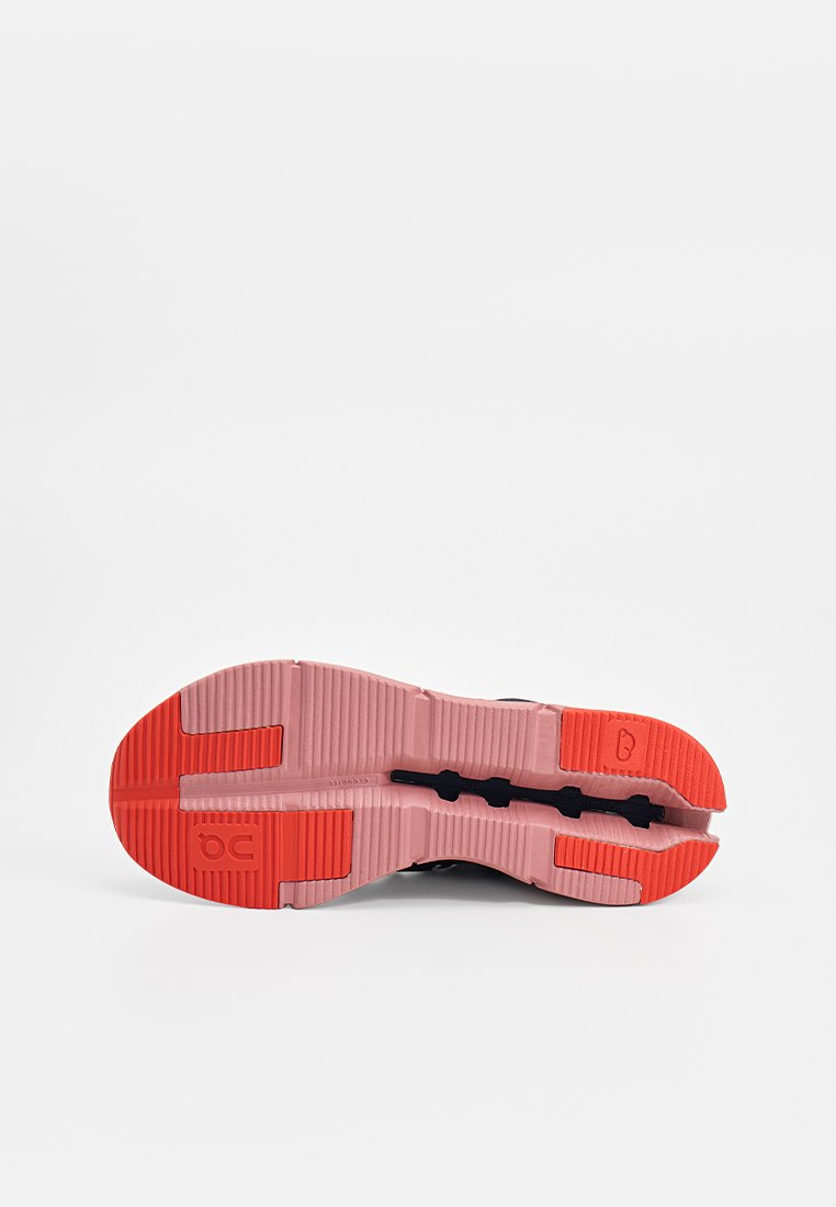 Zool van een hardloopschoen met een roze en rode rubberen profiel en zwarte flexgroeven op een plain witte achtergrond.