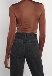 Ruskea pitkähihaisen, vartalonmyötäisen yläosa, yhdistetty korkeavyötäröisiin mustiin farkkuihin, joissa on takataskut ja kulutuspinta.