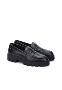 Mocasines de cuero negro con tachuelas plateadas, puntera redondeada y suela de goma gruesa. Accentuados con una correa decorativa sobre el empeine.