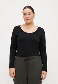 Top negro de manga larga con un escote redondeado, hecho de material suave, combinado con pantalones verdes con cordón. Tejido plano, diseño ajustado.