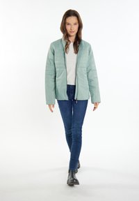 Ljusgrön vadderad jacka med dragkedja fram, med en texturerad quiltad design och vida ärmar. Kombinerad med tajta blå jeans och svarta stövlar.
