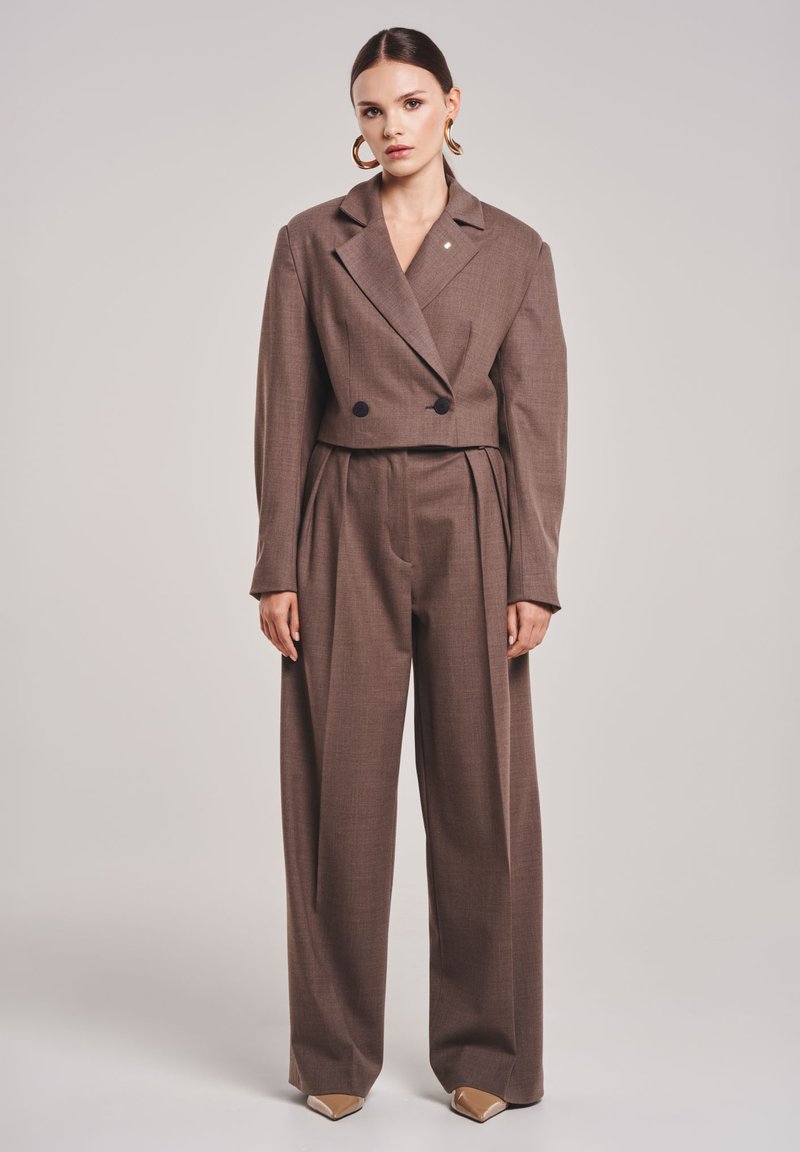 Bruin op maat gemaakte cropped blazer met dubbele zwarte knopen, gecombineerd met losse bruine broek. Soepele textuur en gestructureerd ontwerp. Chunky gouden oorbellen.