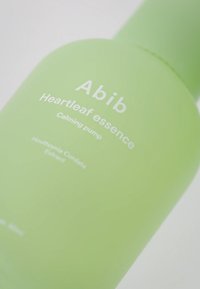 Zielona butelka z matowym wykończeniem i pompką, z białym napisem: "Abib Heartleaf essence Calming pump" oraz listą składników poniżej.