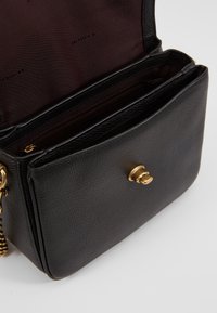 Borsa in pelle nera con una texture granulosa, dotata di una chiusura dorata e una tasca con zipper all'interno. Foderata in tessuto borgogna scuro.