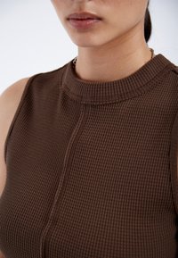 Débardeur côtelé marron avec un col montant et un tissu texturé, présentant des détails de couture visibles et sans manches.
