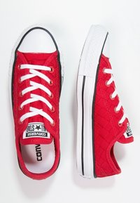 Zapatillas de lona rojas con textura acolchada, suelas de goma blanca y cordones. Presentan una franja lateral negra y el logo de All Star en la lengüeta.