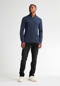 Marinblå pullover med kvartszipp och texturerat tyg, långärmad med ribbade muddar, kombinerad med svarta byxor och vita sneakers.