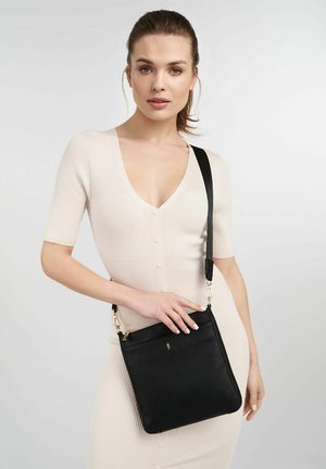 Czarna skórzana torba typu crossbody o fakturowanym wykończeniu. Posiada górne zapięcie na zamek, regulowany pasek oraz akcenty w kolorze złotym.