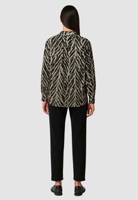 Camicia a maniche lunghe con un motivo a zebra nero e oro, colletto, vestibilità ampia. Indossata con pantaloni neri e scarpe nere senza lacci.