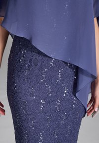 Robe bleu marine avec une superposition transparente et une jupe en dentelle ajustée ornée de sequins, créant un effet texturé et superposé.