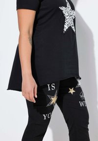 Zwarte t-shirt met een grote paillettenster; gecombineerd met zwarte broek versierd met bedrukte tekst, sterren en strass-accenten.