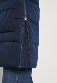 Granatowa pikowana kurtka z bocznym zamkiem błyskawicznym i zapięciem na guziki, o gładkiej fakturze i puchatym kroju.