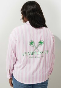 Röd och vit randig långärmad skjorta med en grön grafik av tennisracketar och palmträd, med texten "CHAMPIONSHIP MALIBU TENNIS CLUB".